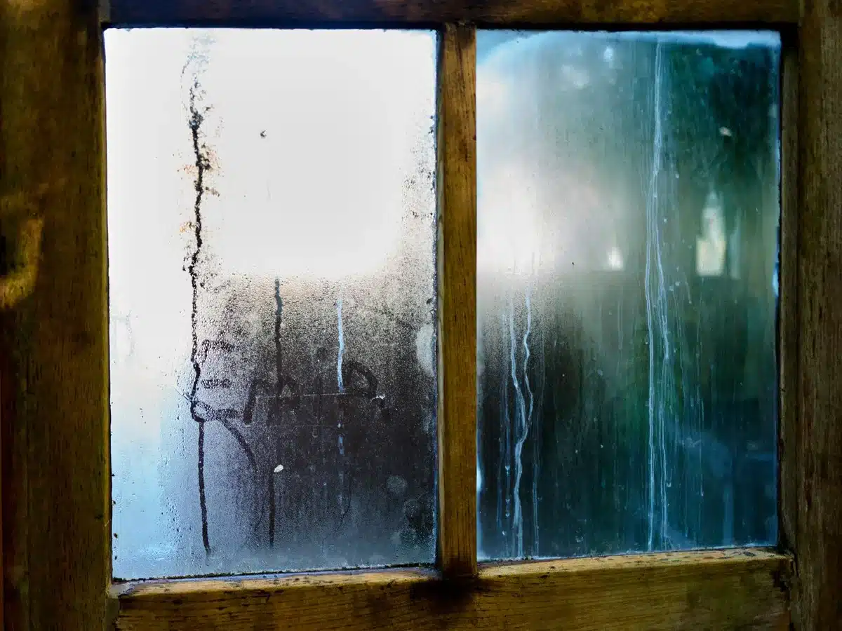 Ancienne fenêtre avec traces d'humidité et infiltrations d'air, montrant les pertes thermiques