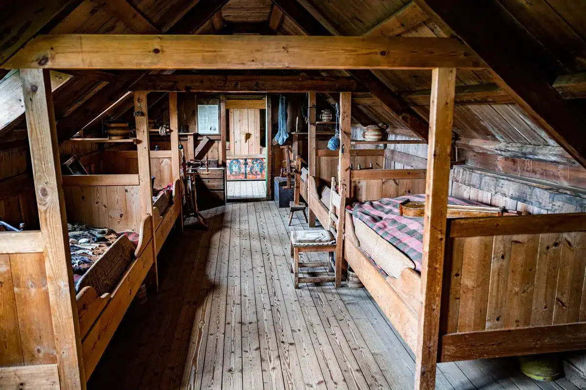 Détails intérieurs d'une maison ancienne : poutres en bois, pierre apparente et plancher usé.