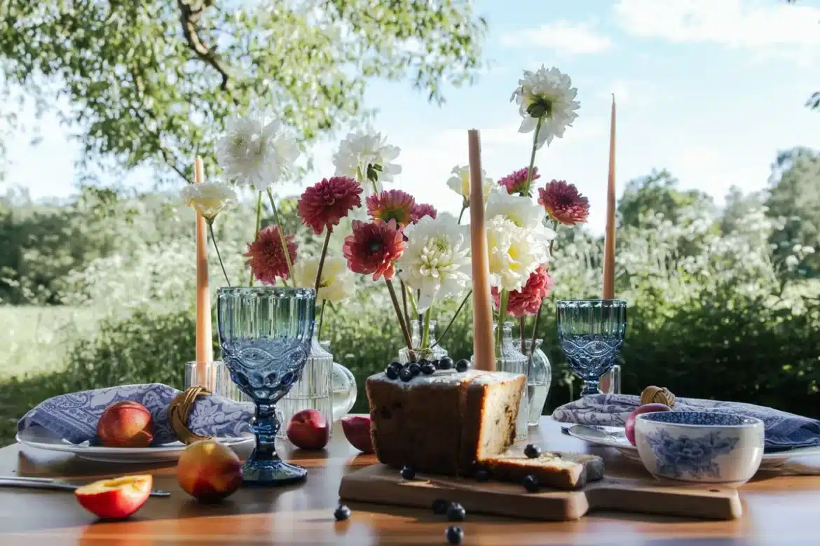 Table d'été avec vaisselle florale, bougies parfumées et éléments botaniques en lumière naturelle