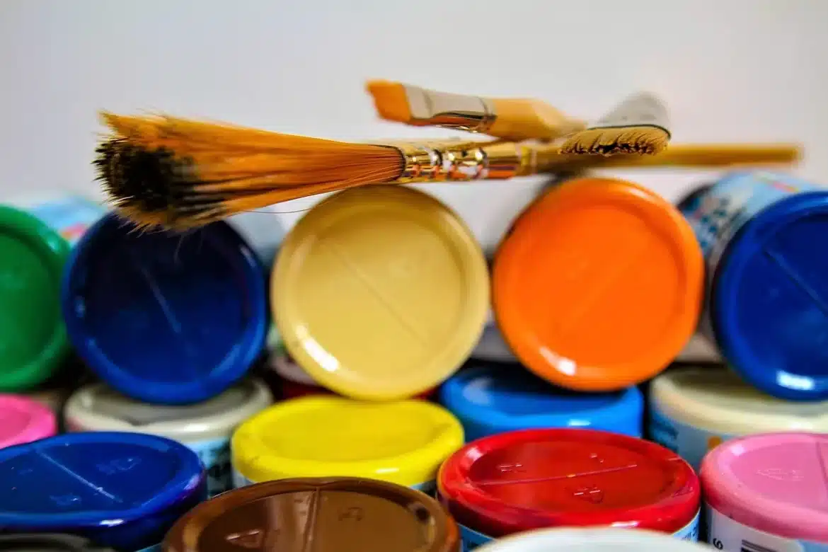 Mains appliquant la peinture sur un meuble en bois avec pinceau et outils de préparation