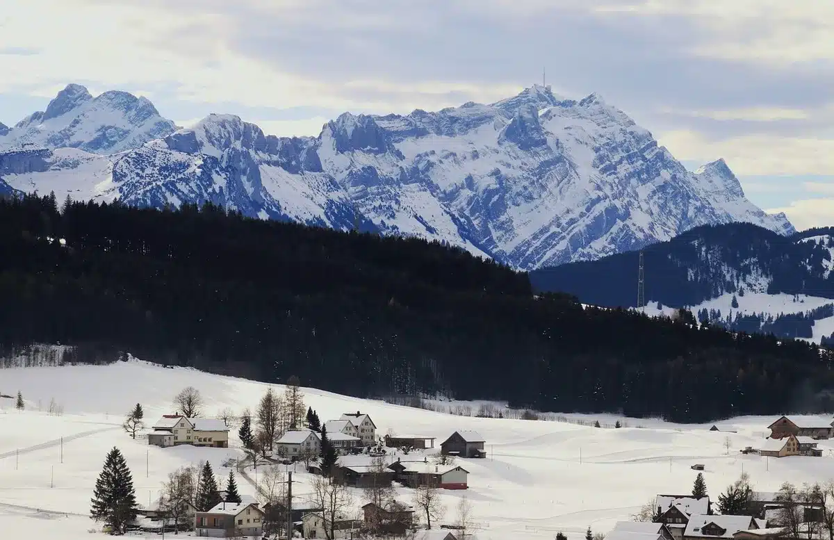 Village sur plateau ouvert avec prairies et montagnes au loin